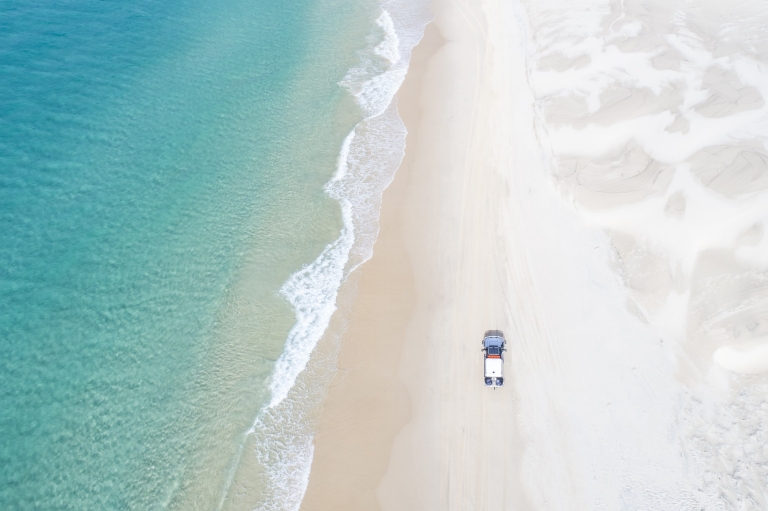 Ảnh chụp từ trên không một chiếc xe 4WD đang chạy dọc bãi biển trên Đảo K'gari, Queensland © Tourism and Events Queensland